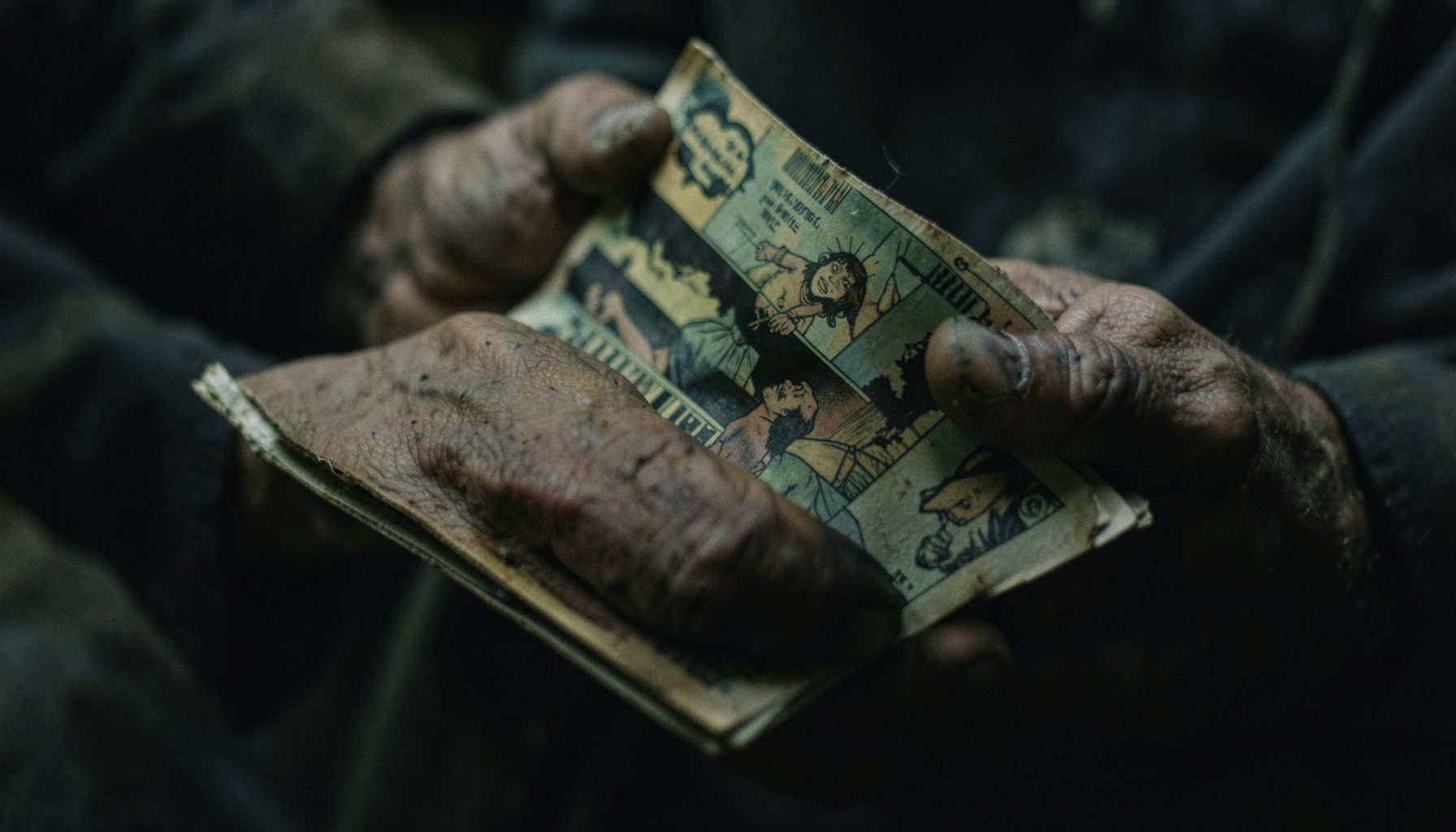 A dim, atmospheric close-up of weathered hands holding a worn comic book, muted greens and browns dominating the scene