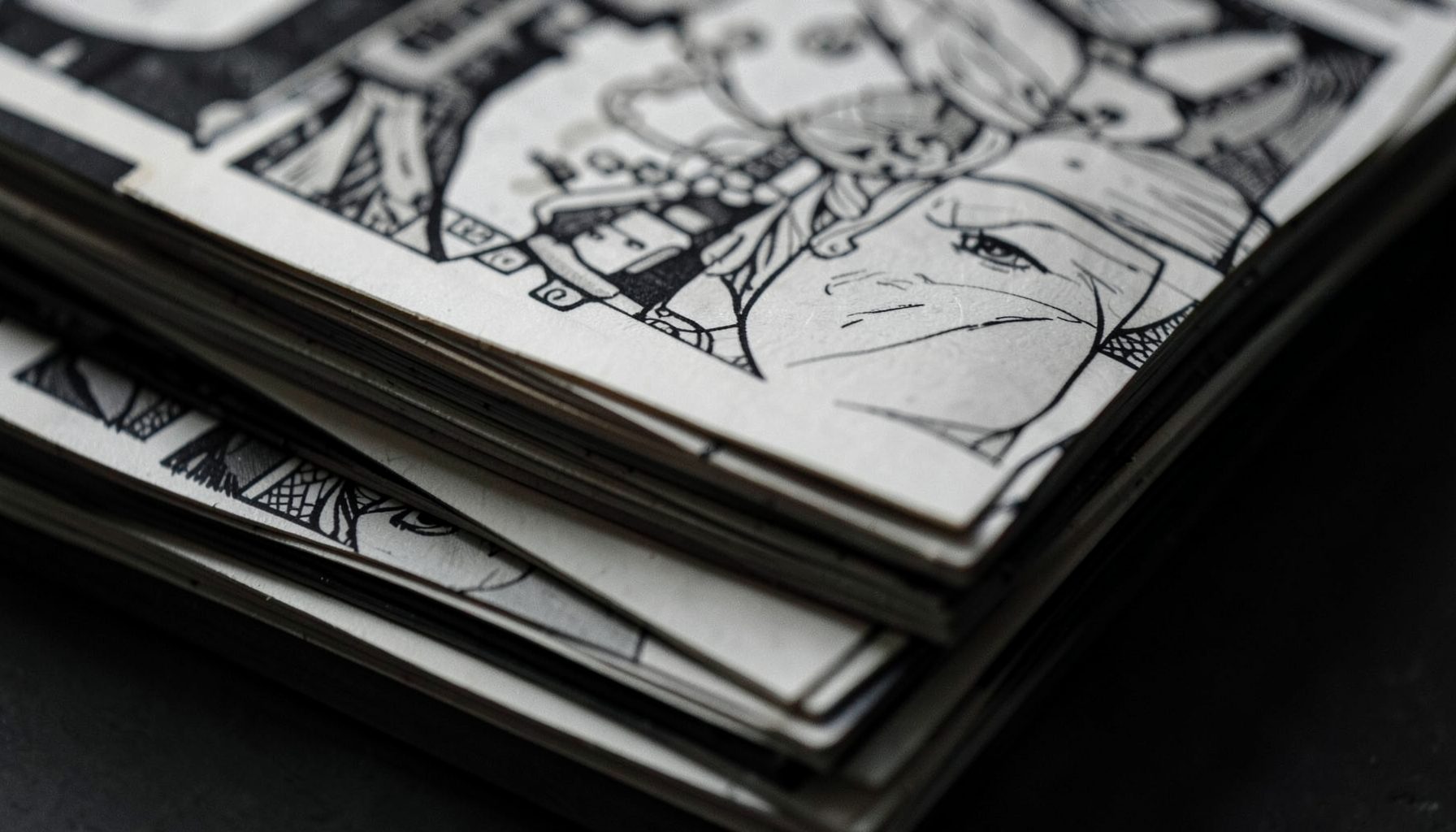 A moody, desaturated close-up of stacked comic book pages with black-and-white line art visible, dark grays and muted tones